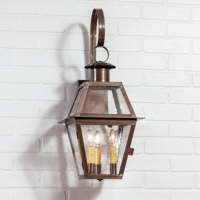 Bronze outdoor wall lantern with glass cover on a white brick wall