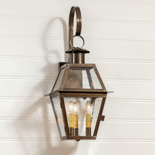 A solid weathered brass outdoor wall light with a blackened solder and a black metal frame, featuring a glass globe and hanging from a circular metal rod.