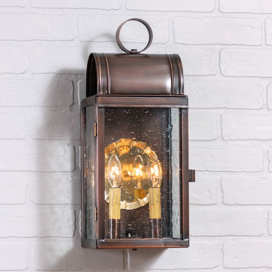 A wall-mounted outdoor wall light with a solid antique copper finish, featuring a clear glass globe and two visible bulb sockets inside.