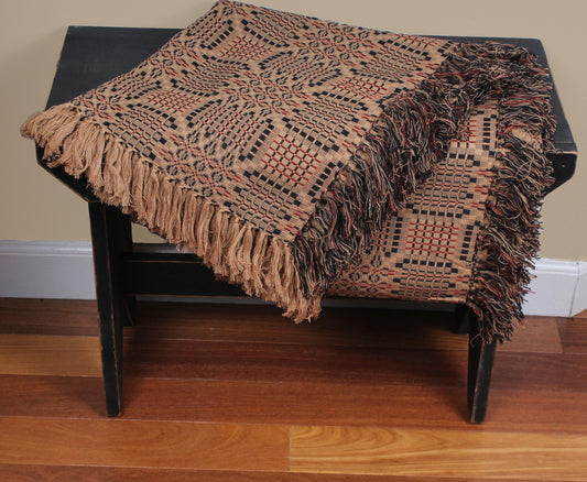 A tri-color jacquard afghan with patterns, displayed on a dark wooden chair, in shades of brown, black, and red.