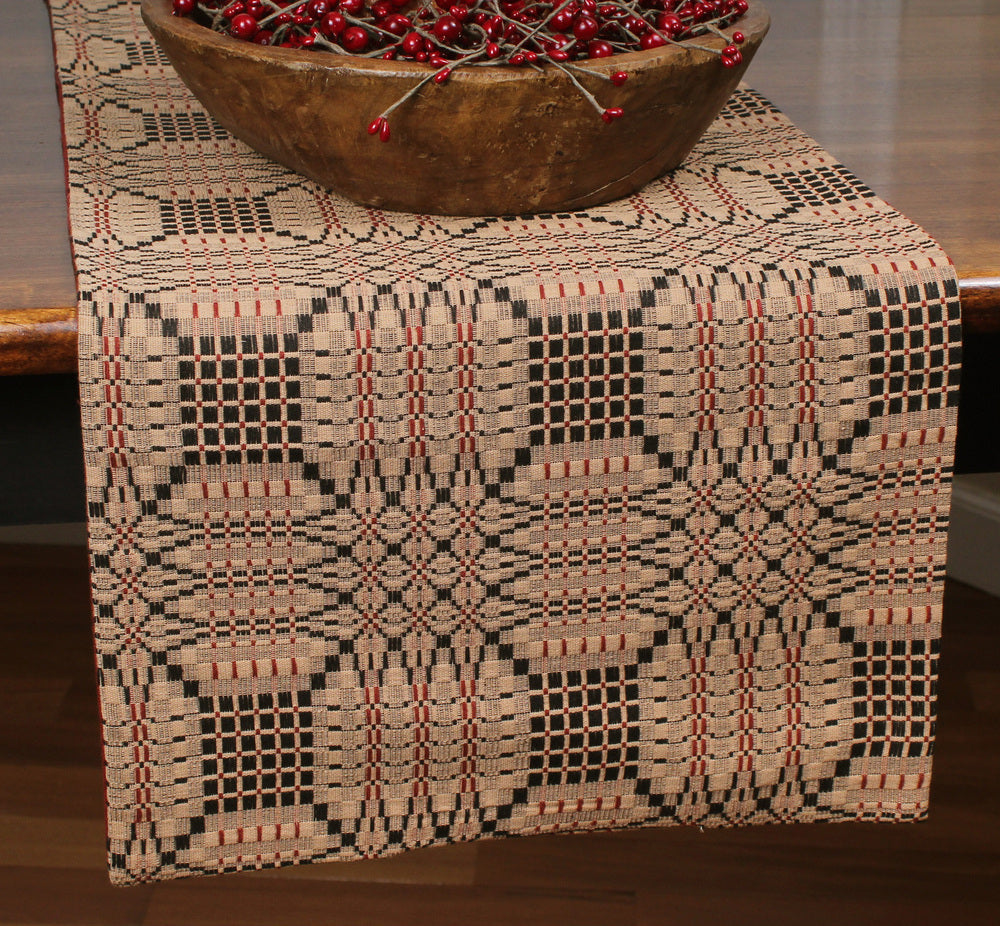 A jacquard table runner with a geometric pattern in black, red, and beige colors, displayed on a table.