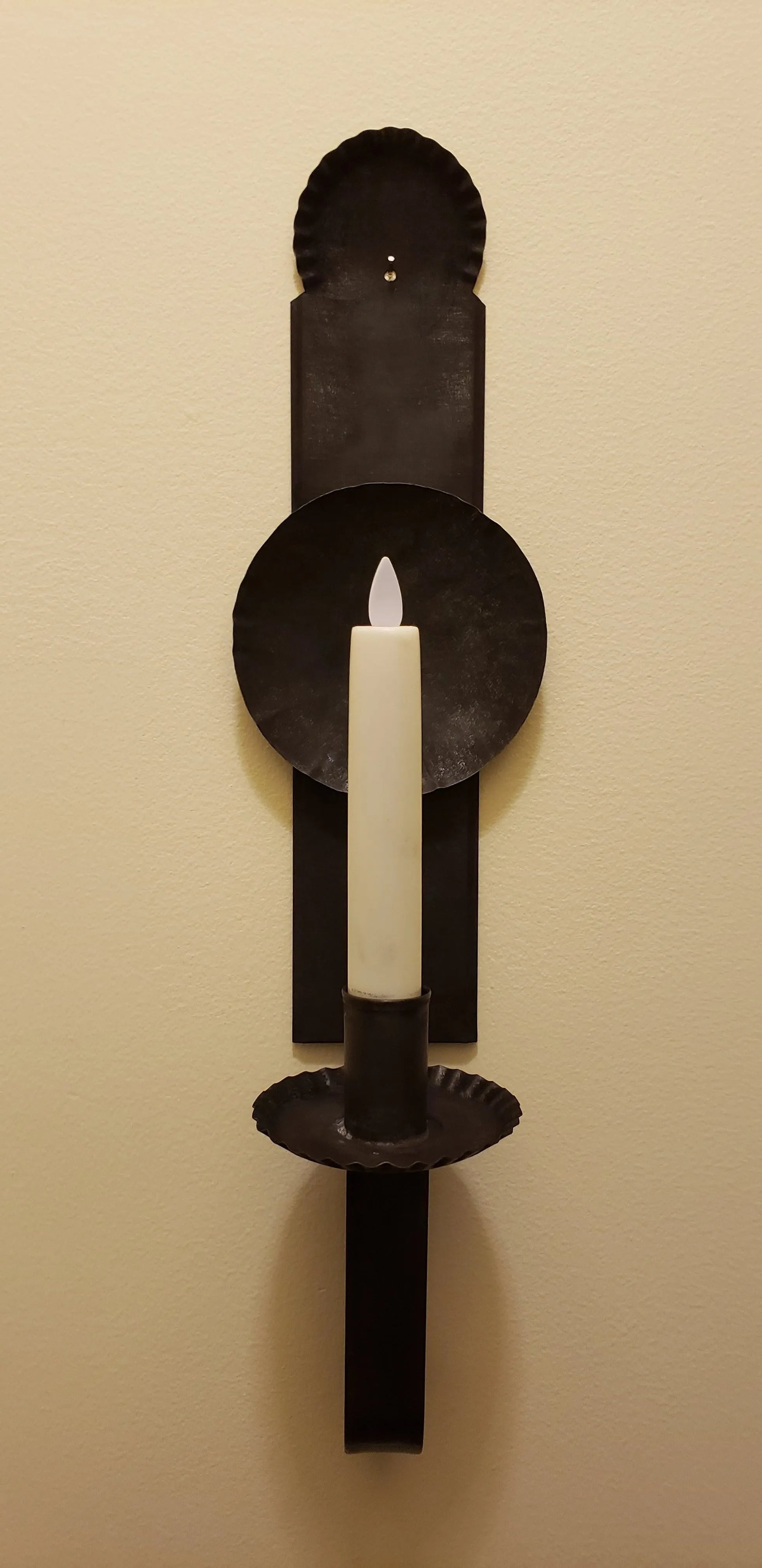 A black metal candle sconce with a primitive finish, hanging on a wall. It features a candle holder at the top.
