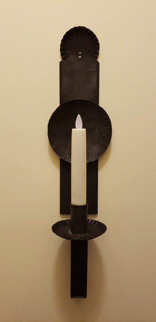 A black metal candle sconce with a primitive finish, hanging on a wall. It features a candle holder at the top.