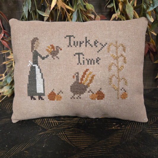 Cross-stitched pillow with 'Turkey Time' text and illustrations on a textured surface.