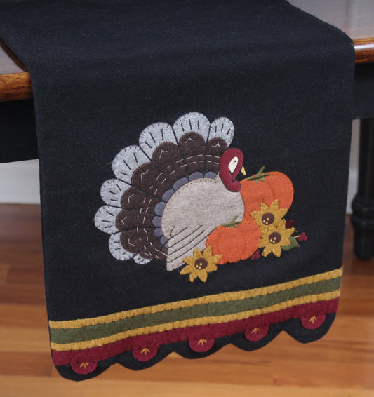 A black wool felt table runner with a turkey design accompanied by autumn-themed decorations, displayed on a dining table.