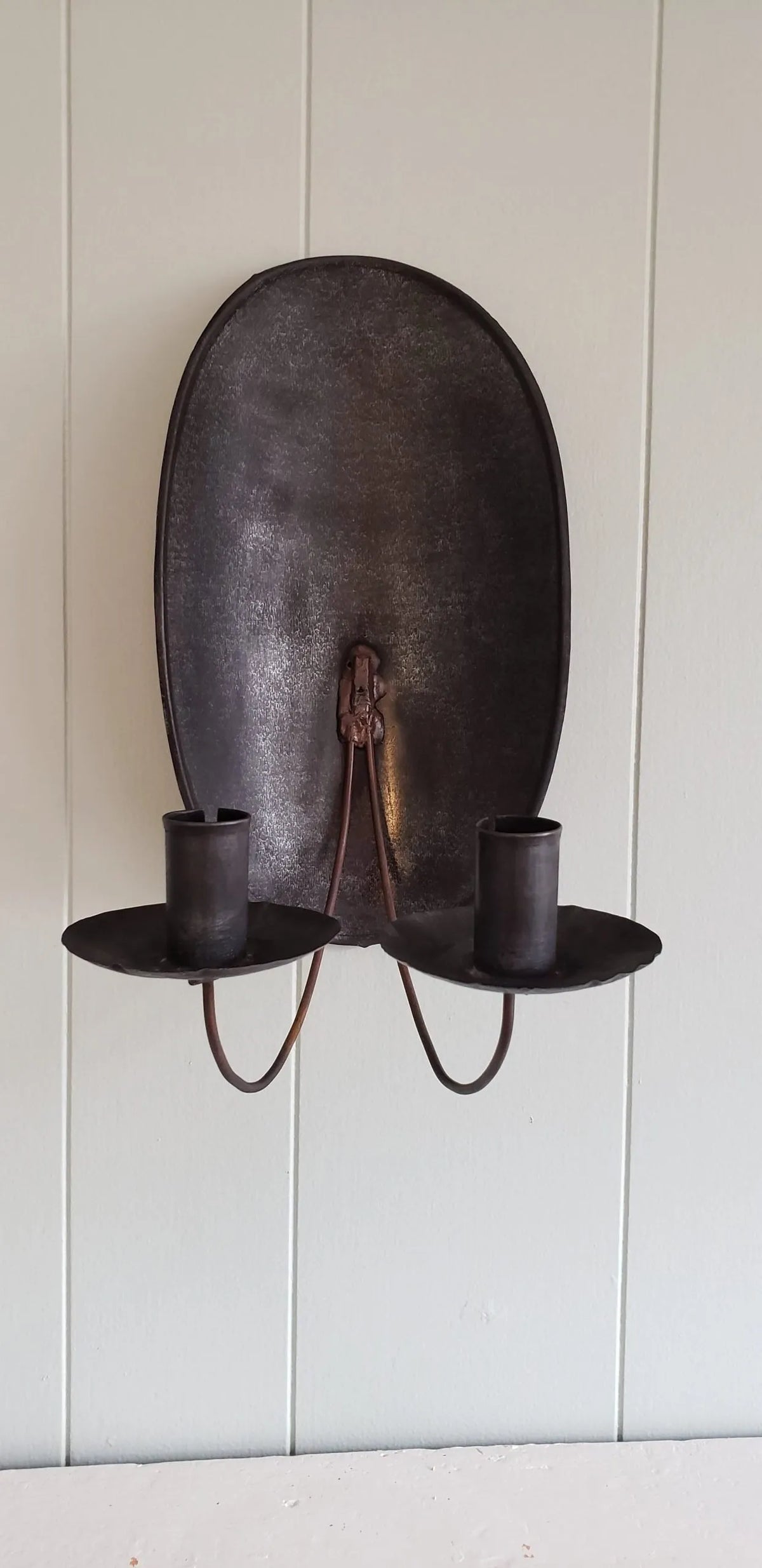 Tin sconce with two candle holders on a white wall.