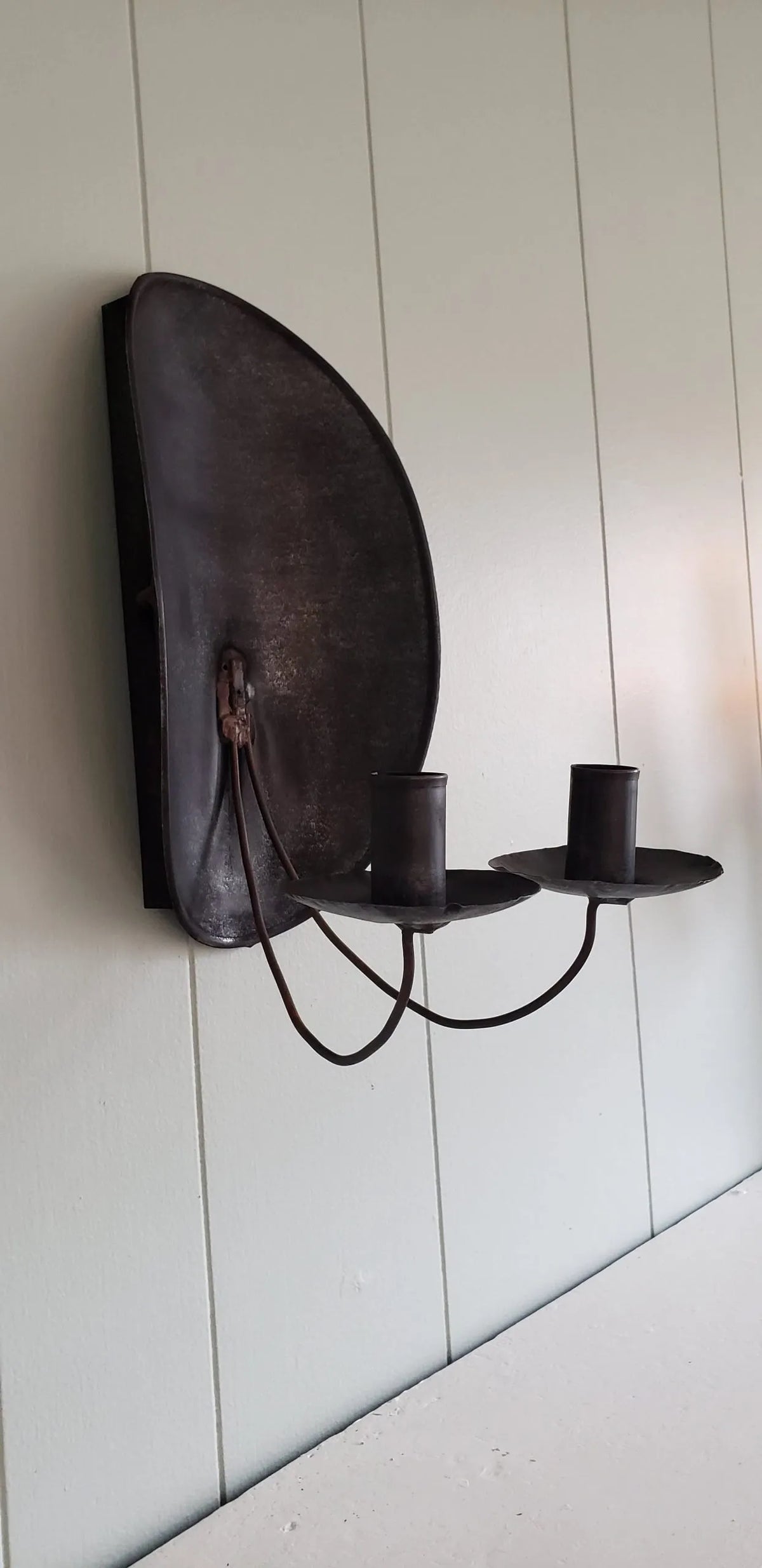 Side view of tin sconce with two candle holders on a white wall.