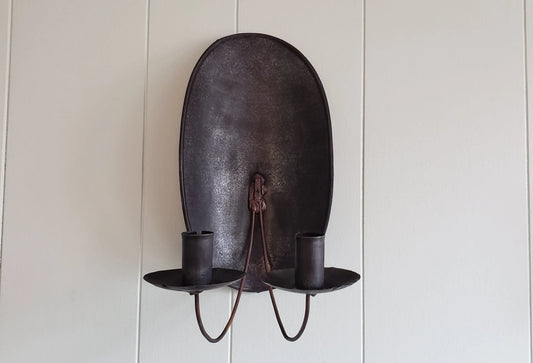 A brown metal turtleback tin candle sconce mounted on a wall, with two candle holders.