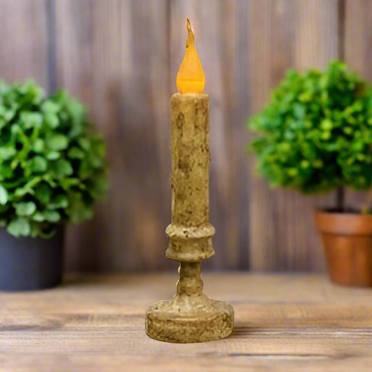 Flickering candle in a decorative holder on a blurred background with greenery beside it