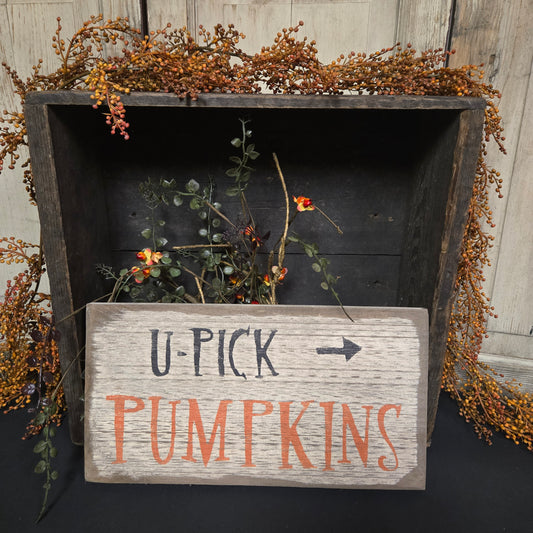 Wooden sign with 'U-Pick Pumpkins' text on a rustic wooden surface with foliage.