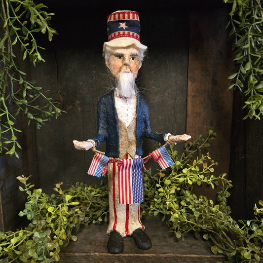 Decorative figure of Uncle Sam holding American flags on a wooden surface with green foliage.