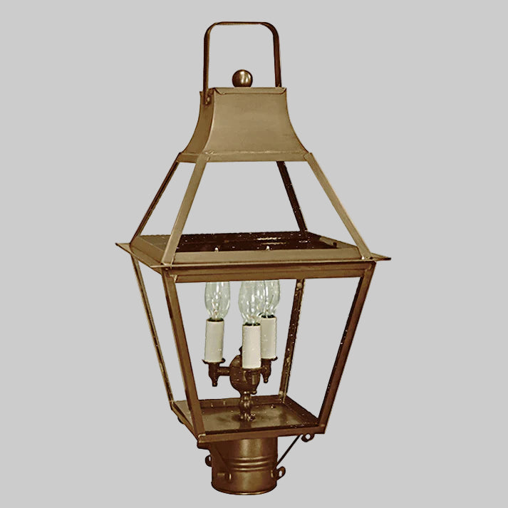 Brass outdoor post lamp with three light bulbs on a gray background