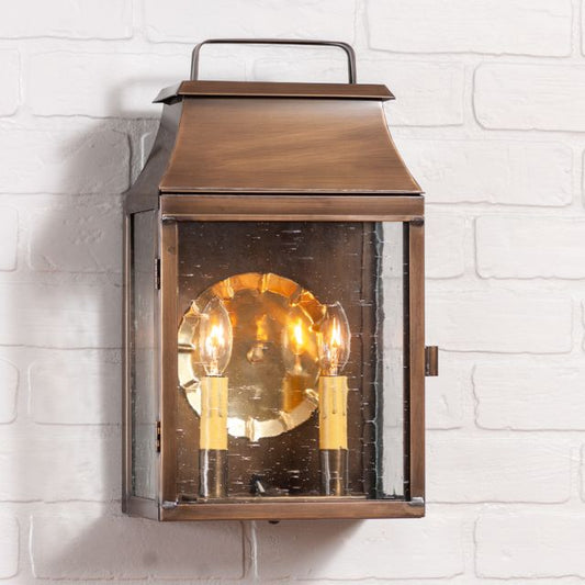 Colonial brass wall light with two candelabra bulbs and bubbly glass on a white brick wall.