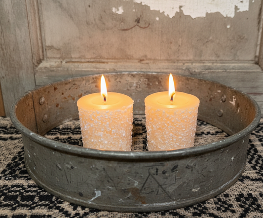 Two lit candles in a rustic metal container on a textured surface.