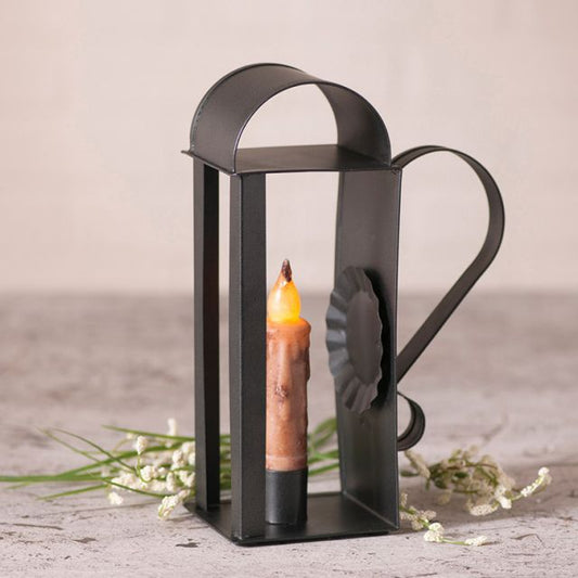 Tin candle holder that accommodates a real or battery operated taper candle with flowers in background.