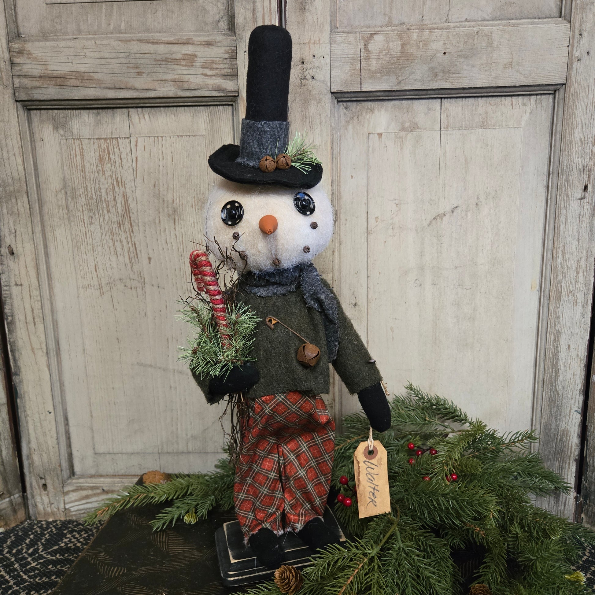 Decorative snowman figure with a tag next to a Christmas wreath on a wooden door.