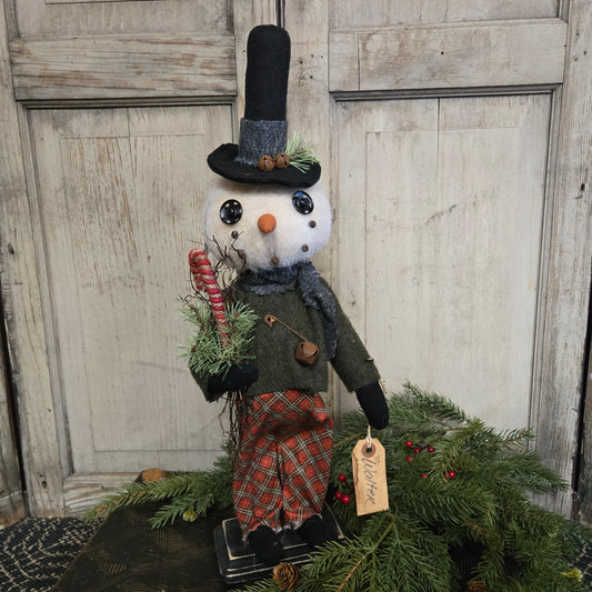 Decorative snowman figure with a tag next to a Christmas wreath on a wooden door.