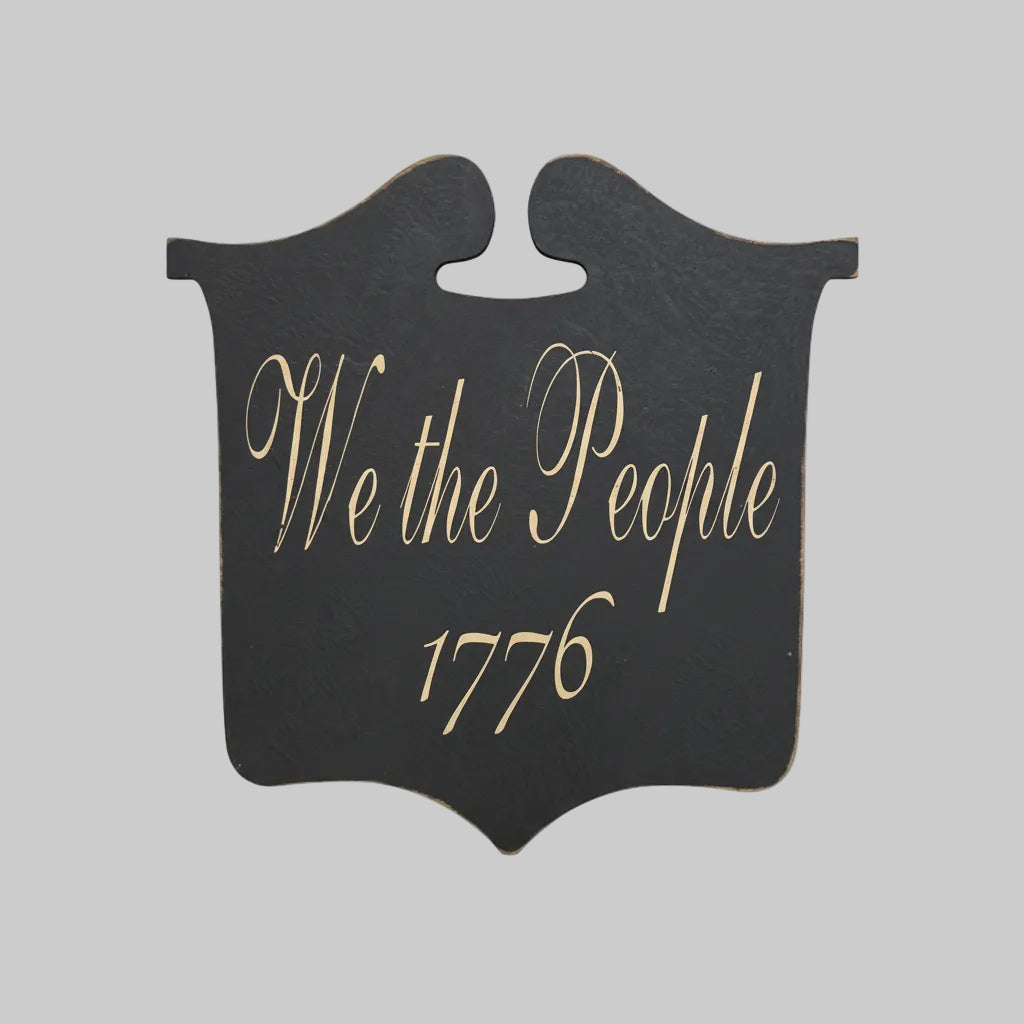 Decorative sign with 'We the People 1776' text on a wooden surface