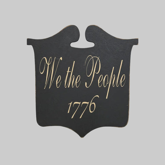 Decorative sign with 'We the People 1776' text on a wooden surface
