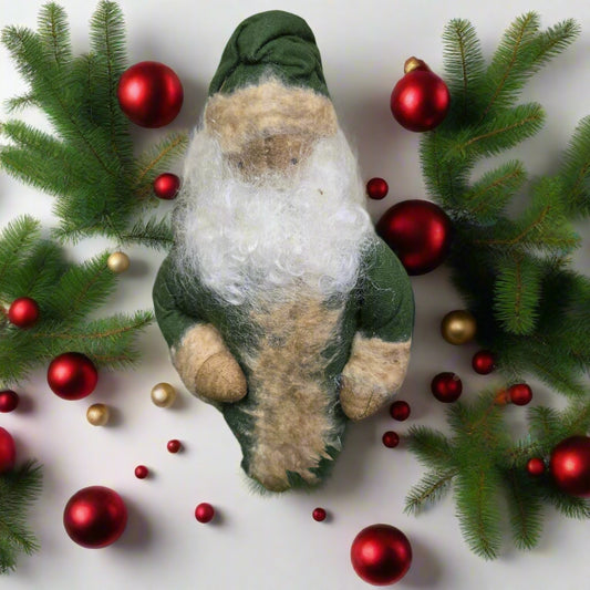 Felted Santa surrounded by greenery and berries on a wooden surface