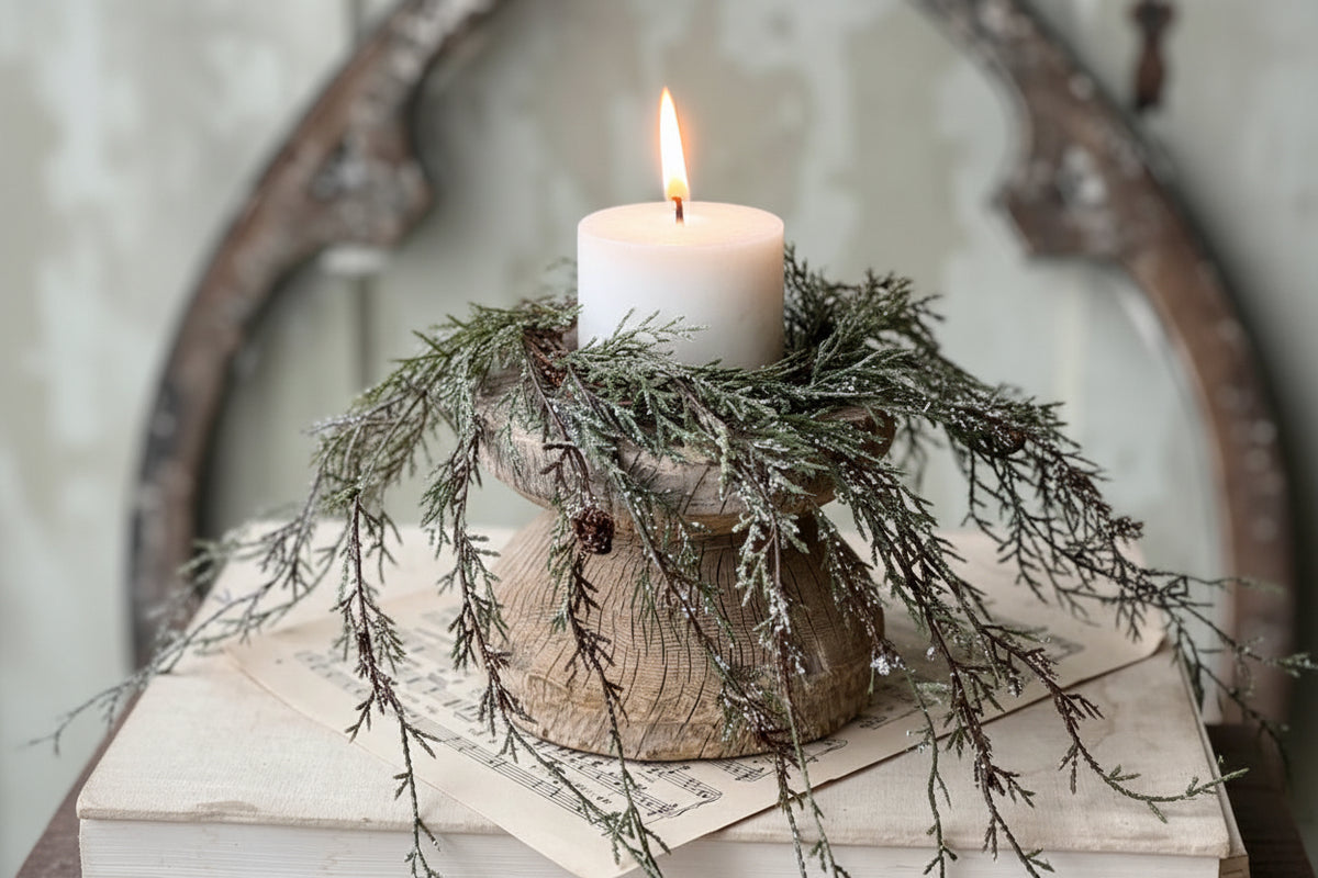 Decorative candle on a wooden block with greenery against a rustic background