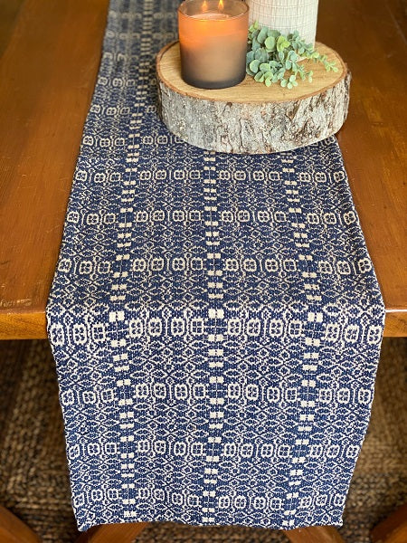 A navy and linen short table runner with a geometric pattern, displayed on a table with a candle and decorative items.