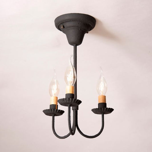 Black three-armed chandelier with lit candles on a light pink background