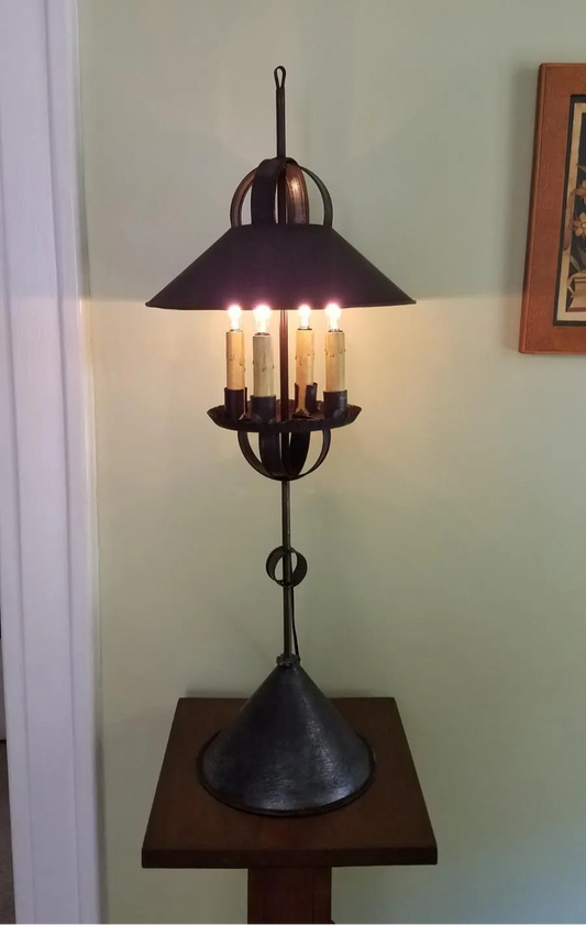 A tall tin table light with a black shade and base, featuring four visible bulb sockets.