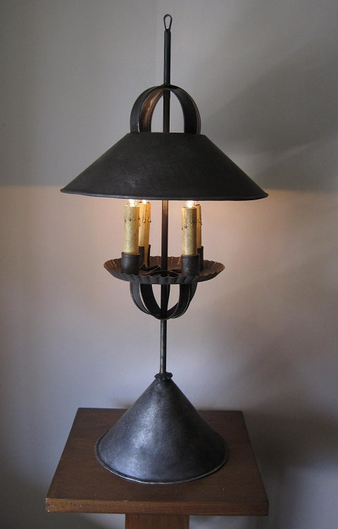 A Weston Tin Table Light with a metallic shade and base, featuring four candle-like light bulbs, placed on a wooden surface.