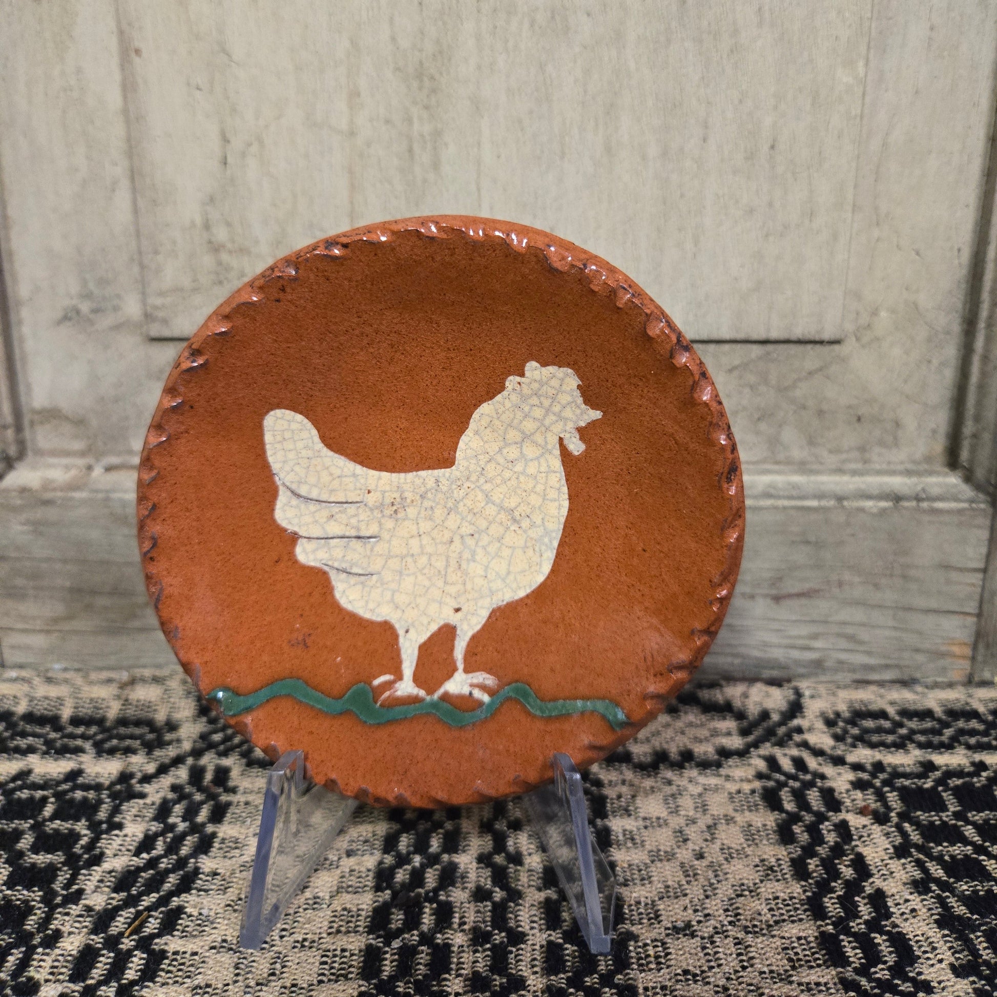 Small round redware plate with a white chicken and a green squiggly line