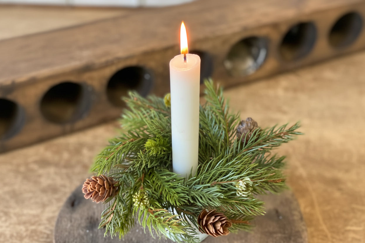 White candle in a holder with greenery on a wooden surface