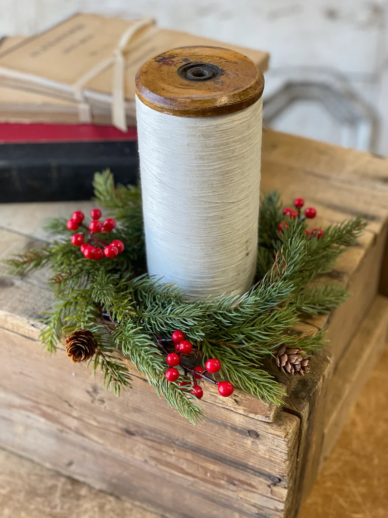 Spool of white thread on a wooden block with greenery and red berries