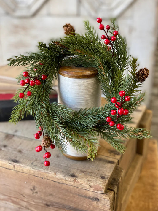 Decorative wreath with greenery, red berries, and pinecones on a wooden surface.