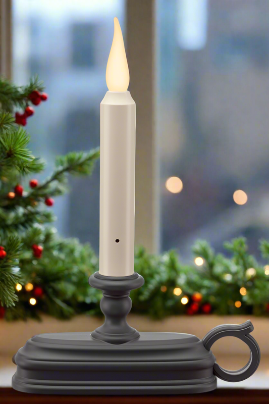 Decorative candle with a gray base in front of a festive background with lights and greenery.