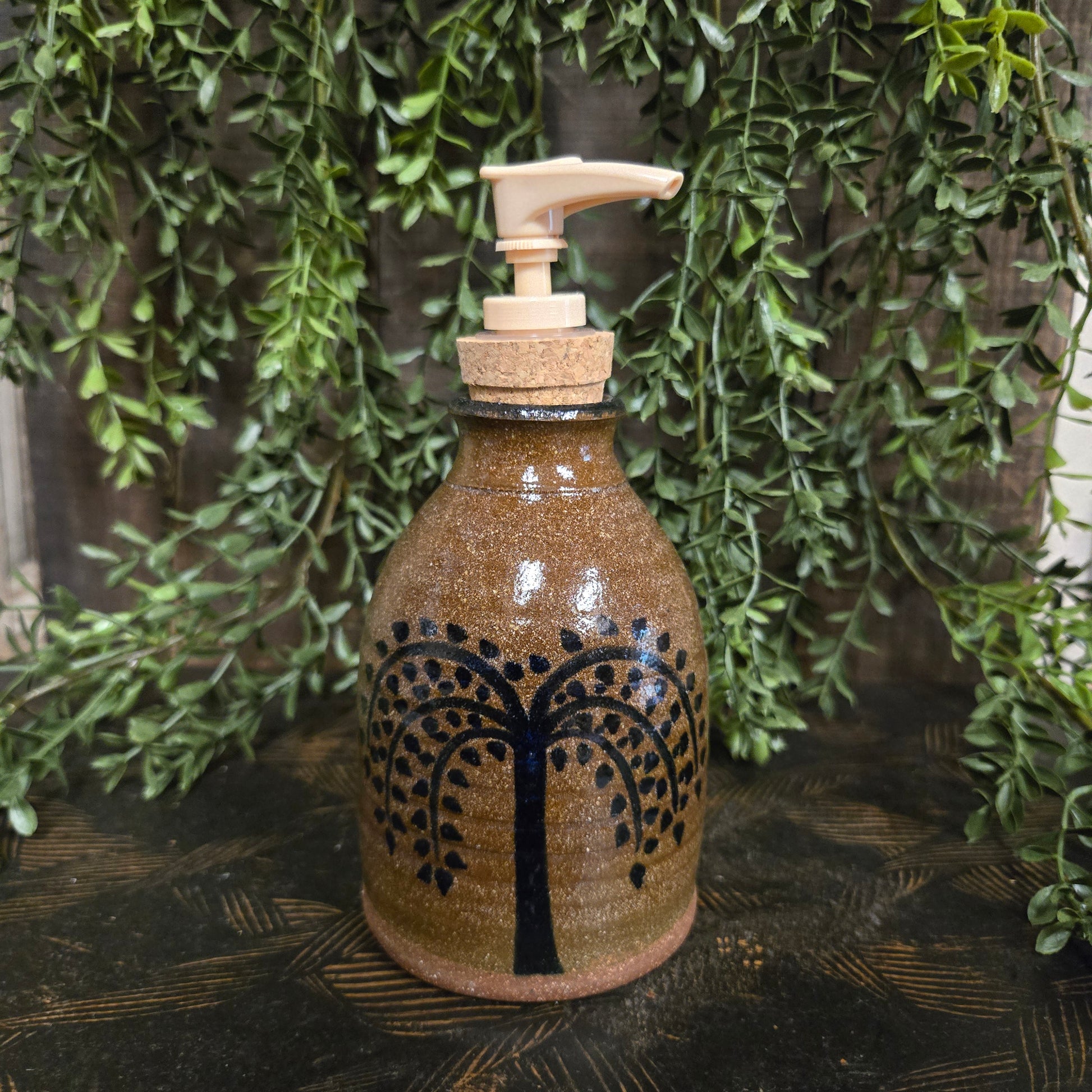 Decorative bottle with tree design on a wooden surface with greenery