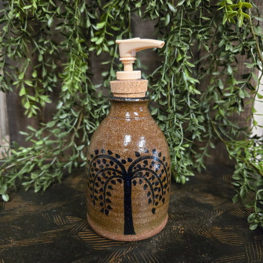 Decorative bottle with tree design on a wooden surface with greenery