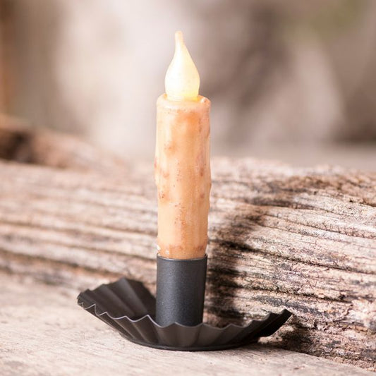 A beige candle placed in a smokey black metal candle holder, which is resting on a wooden surface.