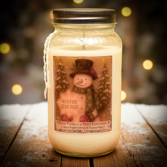 Jar candle labeled 'Winter Star Dust' with a snowman design on a wooden surface.
