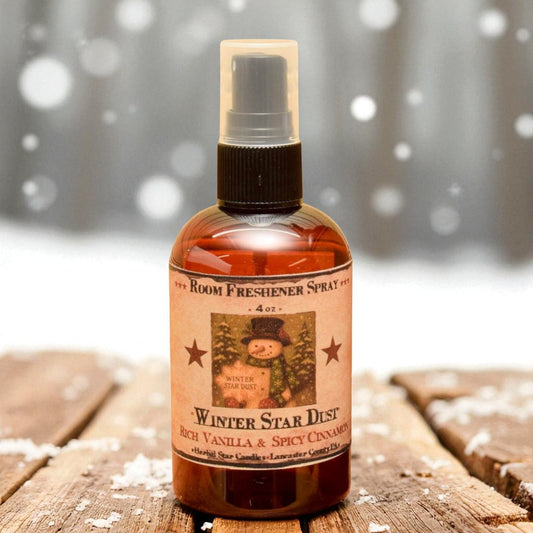 Room freshener spray bottle labeled 'Winter Star Dust' on a wooden surface with a snowy background.