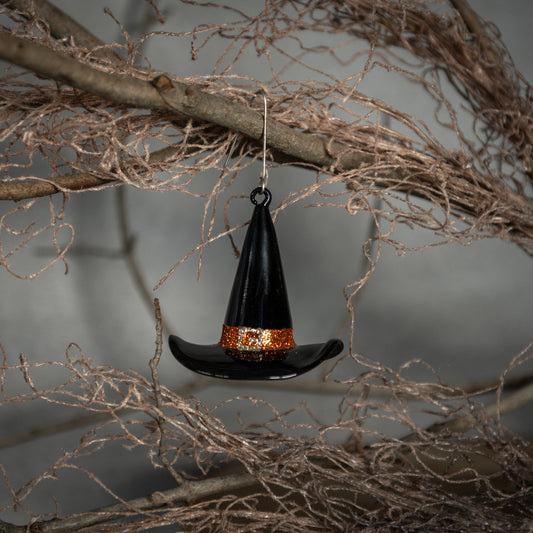 Hanging witch hat ornament on a branch with a gray background