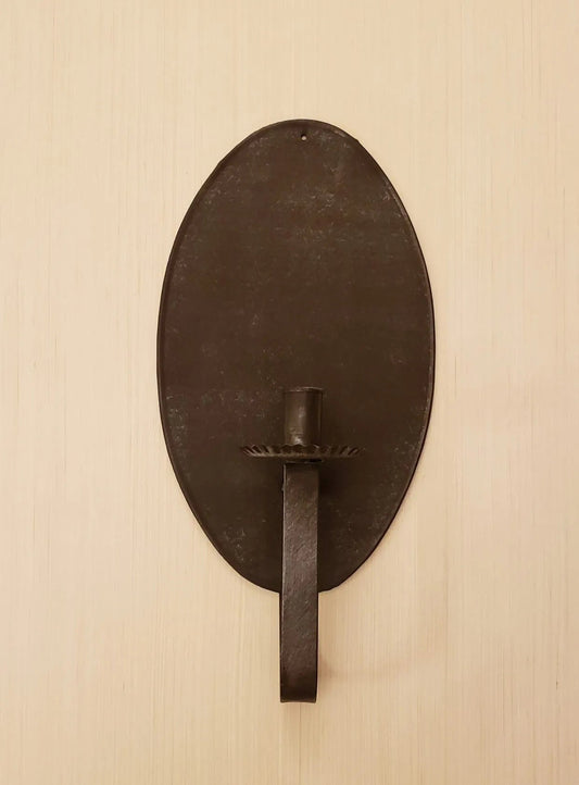 A brown tin candle sconce mounted on a wall, with a reflective surface and a hook for hanging candles.