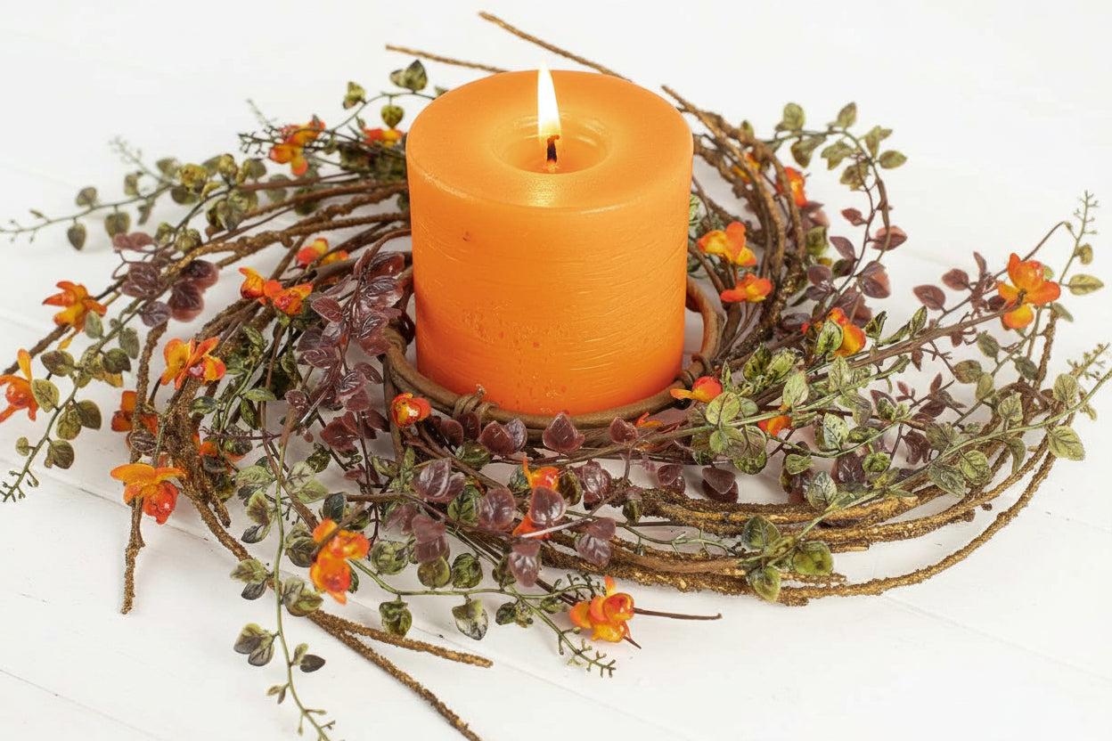 Orange candle in a decorative holder with greenery and small flowers on a white background