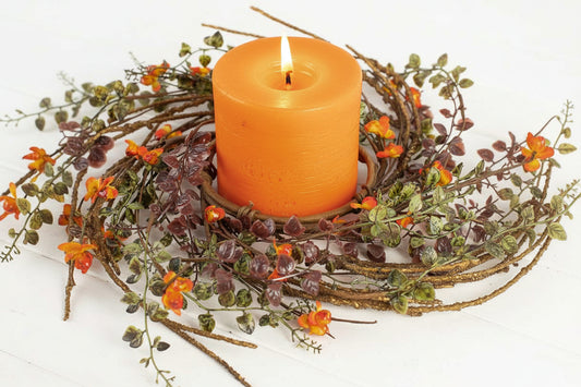 Orange candle in a decorative holder with greenery and small flowers on a white background