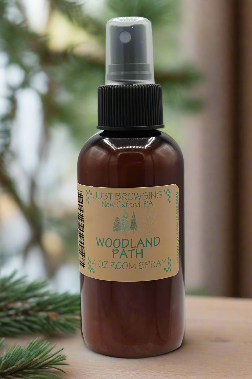 A 4oz bottle of Woodland Path room spray with a mist spray top. The label features the product name and a description 'Wood and pine with hints of sap.