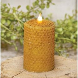 A wrapped honeycomb-textured LED pillar candle with a lit flame, placed on a wooden surface with greenery in the background.