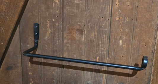 A black metal paper towel holder mounted on a wooden wall.