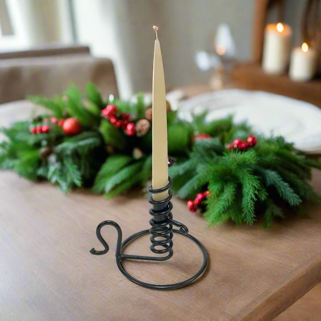 A black wrought iron spiral courting candle holder with a handle and a wide base, designed to hold a candle.