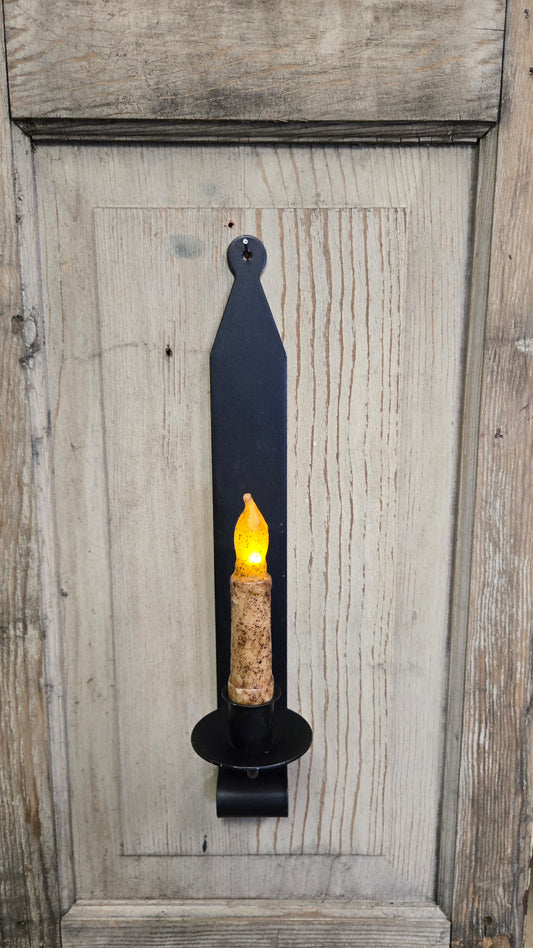 A wrought iron wall sconce mounted on a wooden wall, featuring a black finish and a candle-like light source.