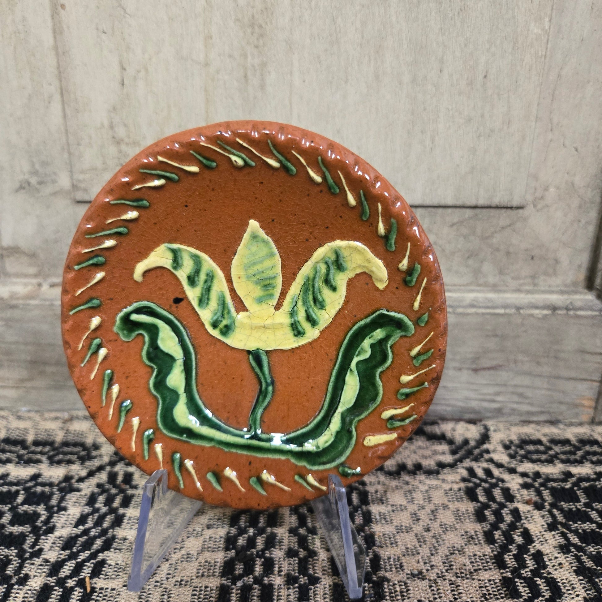 Small round redware plate with a vibrant yellow tulip and an intricate border