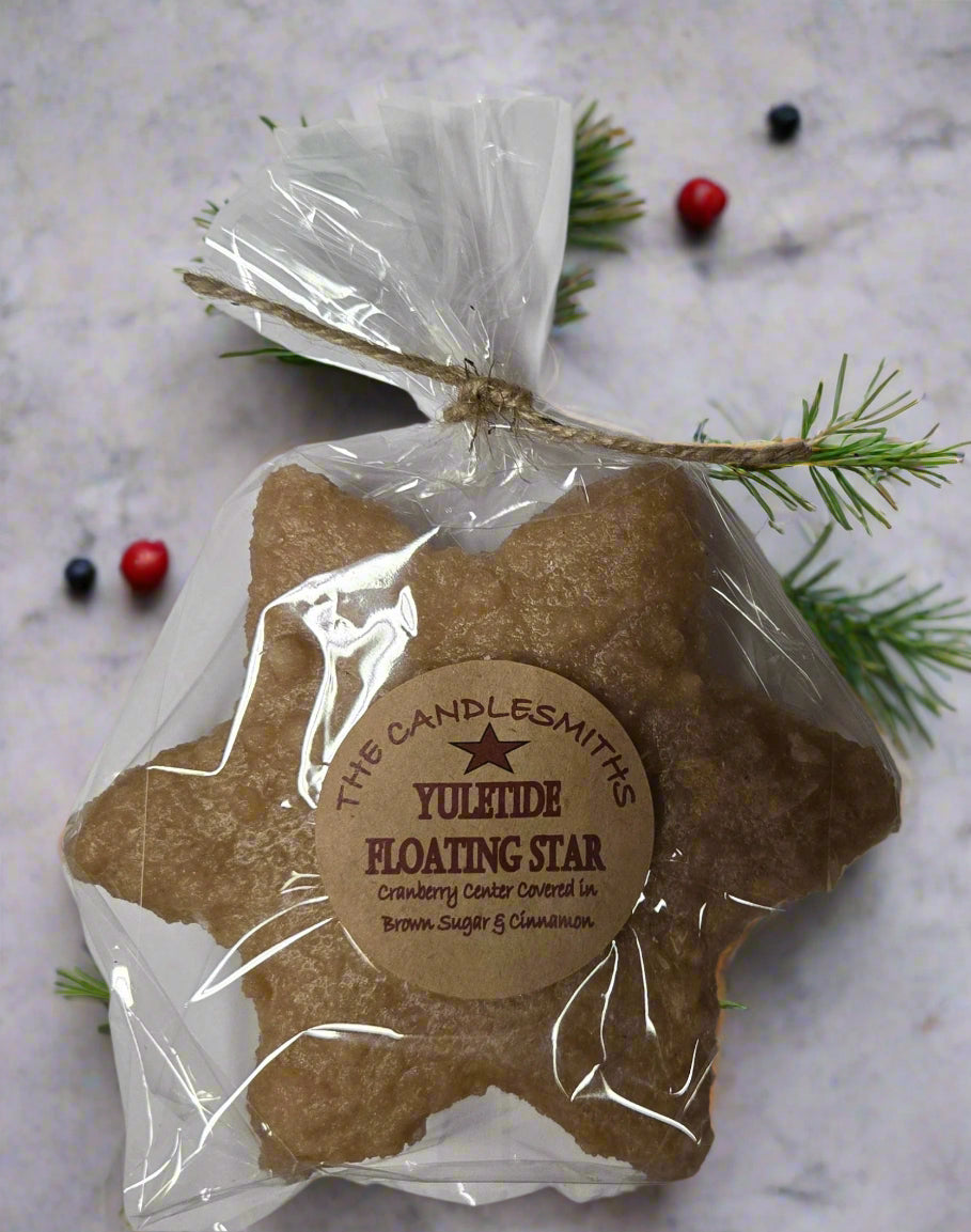 A packaged floating candle designed to look like a star with a cranberry center, dipped in brown sugar frosting, with an oatmeal color. It is wrapped in clear plastic with a label and a string tie.